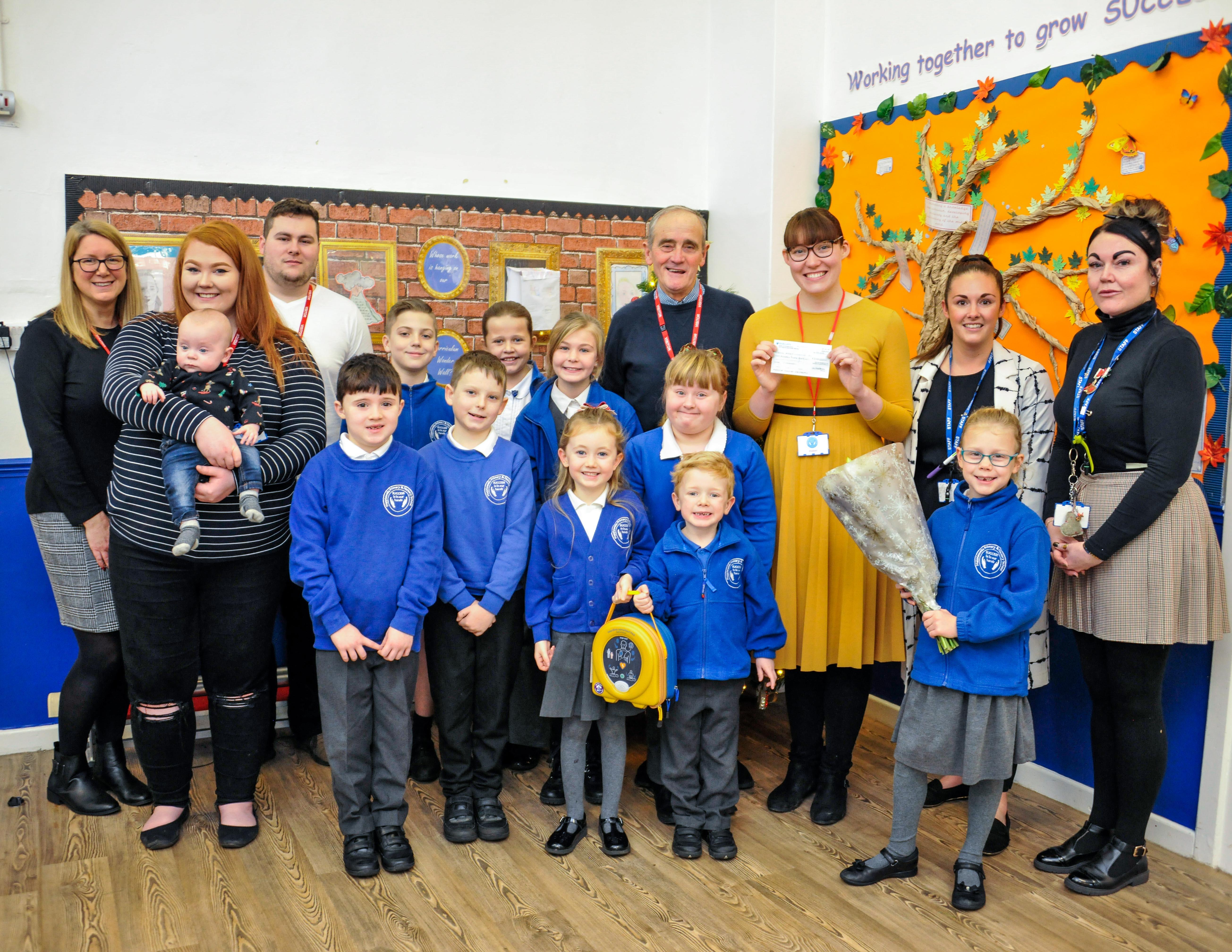 Holly Younger, of Leon’s Legacy, fourth from right,  holds a cheque for £200 donated by Mapplewells Primary and Nursery School, while children hold the new defibrillator now installed at the school.