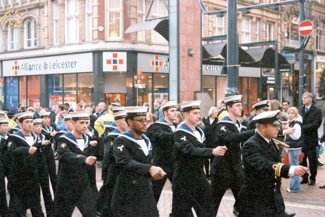 Junior ratings officers from the crew wearing full ceremonial dress, led by a Lieutenant Commander seen on the right. Officers have badges on their right arms which denote their particular job. Rank would be displayed on their left arms. The parade marches along Briggate past the junction with Albion Street.