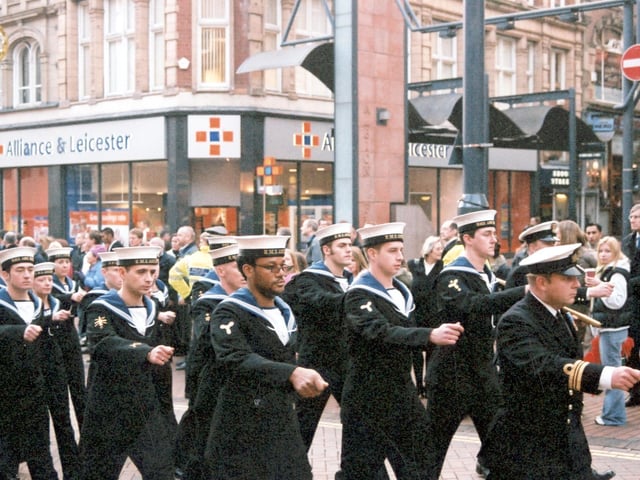 Junior ratings officers from the crew wearing full ceremonial dress, led by a Lieutenant Commander seen on the right. Officers have badges on their right arms which denote their particular job. Rank would be displayed on their left arms. The parade marches along Briggate past the junction with Albion Street.