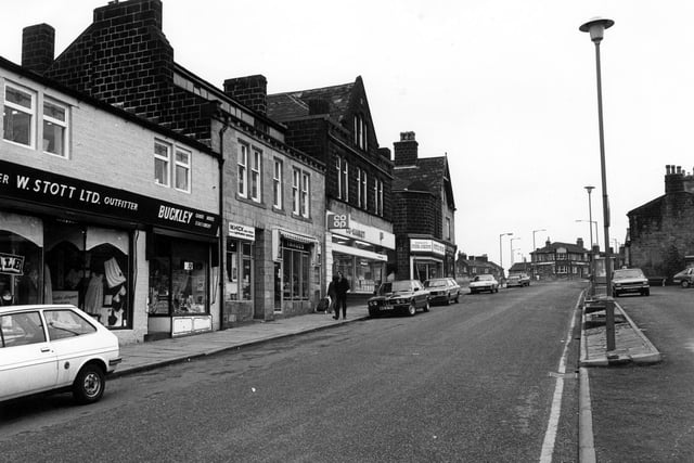 Yeadon High Street in December 1979 looking in the direction of Harrogate Road. On the left shops include W. Stott Ltd, Draper and Outfitter, then Buckley, cards, books and stationery, then M. Hick, optician, followed by Images Hairdressing Salon and the Co-operative store with furniture Salesroom on the first floor next to the junction with Marshall Street. After Marshall Street comes Westfield Top Shop for fish & chips and next door Ben Eastwoods for Carpets. The Albert Inn is visible beyond the junction with Cemetery Road. To the right of the bus shelter is the Clothiers public house.