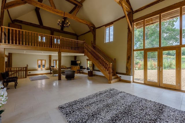 A spacious double-height drawing/sitting room with an exposed stone wall, vaulted ceiling, and stairs rising to a galleried mezzanine level.