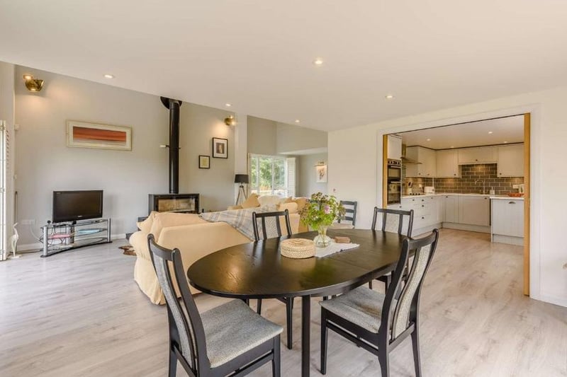 Double-height ceiling and glazing ensure the open plan reception room is filled with natural light, with the seating area centred around a feature wood-burning stove and bi-fold doors opening onto a paved terrace.