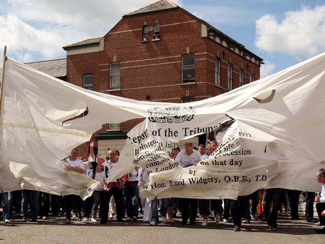Members of the Bloody Sunday Justice Campaign march through a giant copy of the Widgery Report on their way to the Guildhall to hear the findings of the Saville Report.