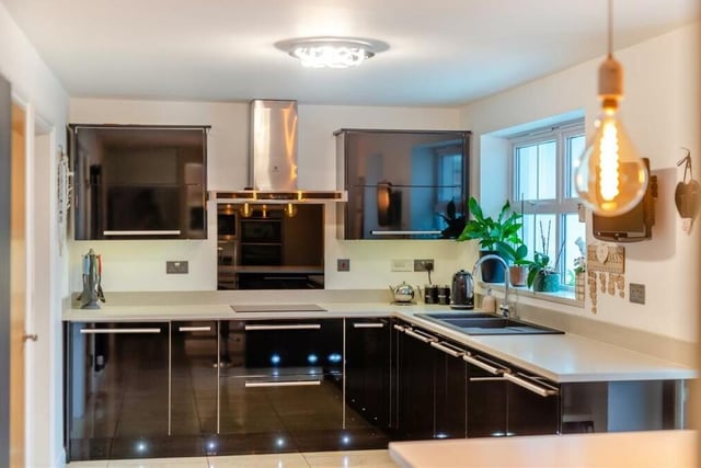 A range of integrated AEG cooking appliances within the kitchen include a stainless steel double oven,, a separate stainless steel microwave, and an induction hob with glass splashback and stainless steel chimney extractor hood above.
