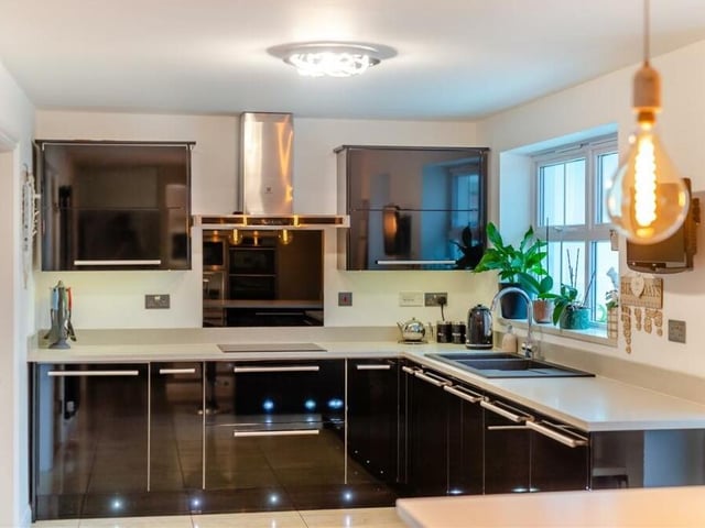 A range of integrated AEG cooking appliances within the kitchen include a stainless steel double oven,, a separate stainless steel microwave, and an induction hob with glass splashback and stainless steel chimney extractor hood above.