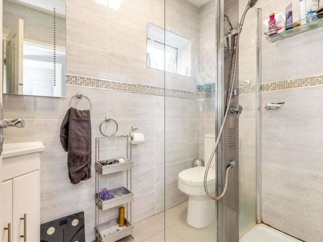 The bedroom in the annexe also has access to this en suite wet room. It features a walk-in shower enclosure, corner vanity unit with inset wash hand basin and storage cupboard beneath, plus a low-flush WC, two fitted mirrors above the sink and a chrome, heated towel-rail.