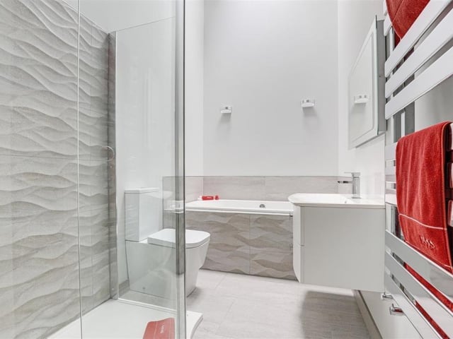 The master bedroom has access to this en suite bathroom. A modern suite comprises a bath with central taps and tiled surround, a shower enclosure with rainfall shower head, a wash basin with storage drawers, and a low-level, dual-flush WC. There is also a vanity mirror that is heated and has lighting, plus a chrome, heated towel-rail and underfloor heating.