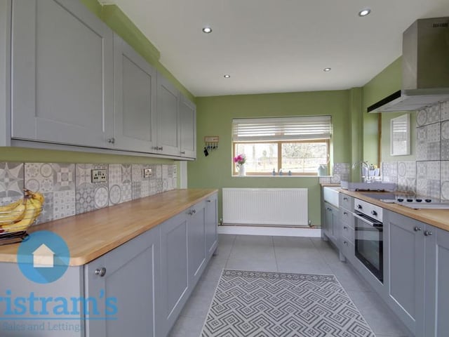 A second view of the lengthy kitchen, which has an integrated fridge freezer and plumbing for a washing machine. There is also a porcelain Belfast sink, which has a chrome Victorian-style mixer tap. Double-glazed doors at the back allow in plenty of light.