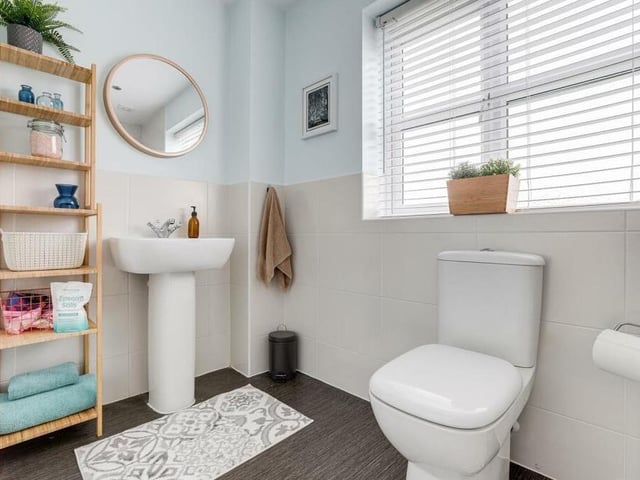 The family bathroom is bright and cheerful, with a pedestal wash basin, storage space, partially tiled walls, recessed spotlights and a vinyl floor.