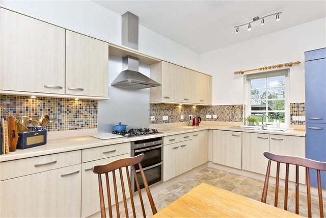 Arranged in an L-shape, the kitchen comes well-appointed with cabinetry and down-lit worktops, framed by mosaic splashbacks.