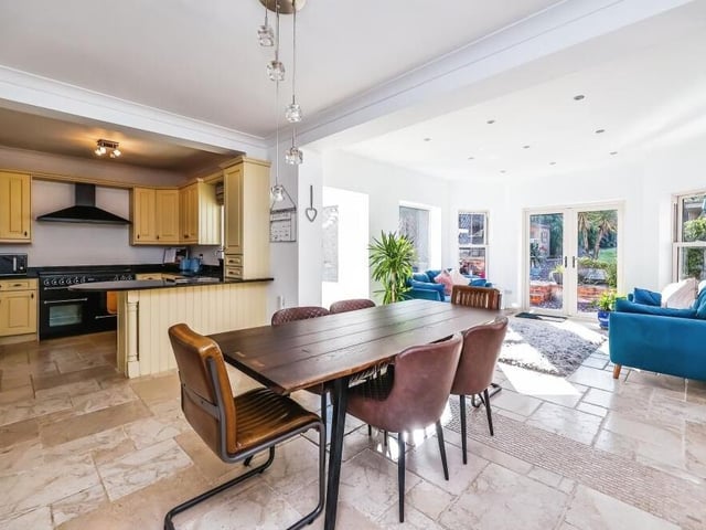 The kitchen forms part of a luxurious open-plan area on the ground floor that flows seamlessly into a dining area (foreground) and a further living space (right).