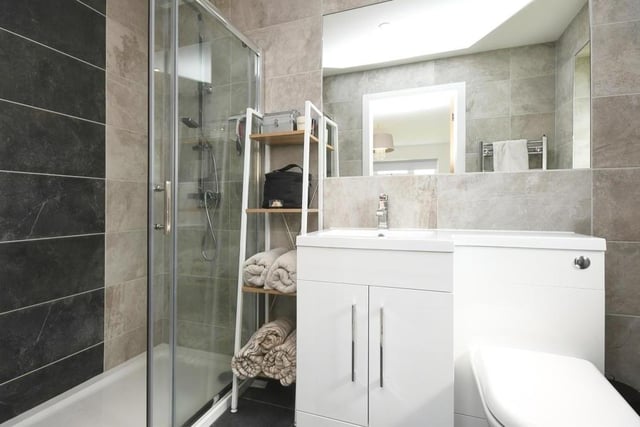 Here is the master bedroom's en suite shower room. It includes a walk-in shower, wash hand basin with vanity unit and mixer tap, WC, fully tiled walls and splashbacks, tiled flooring and a towel radiator.