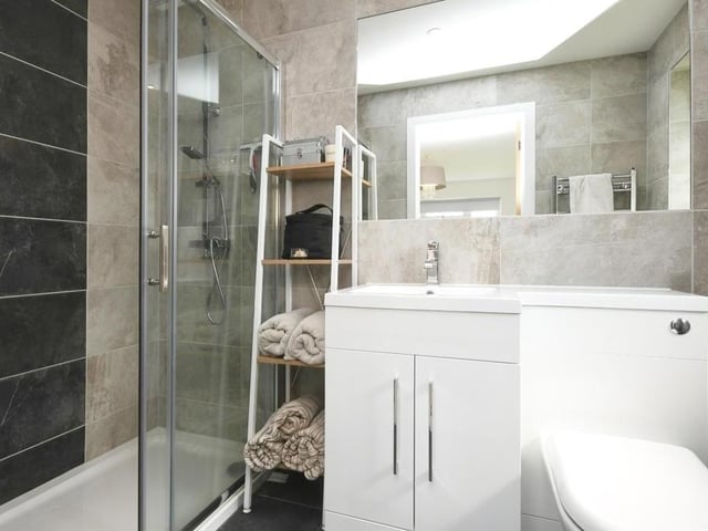 Here is the master bedroom's en suite shower room. It includes a walk-in shower, wash hand basin with vanity unit and mixer tap, WC, fully tiled walls and splashbacks, tiled flooring and a towel radiator.