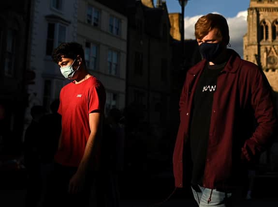 Young men, some wearing a face mask or covering due to the COVID-19 pandemic, walk in the evening sunlight  (Photo by OLI SCARFF/AFP via Getty Images)