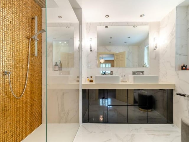 The en suite shower room to the master bedroom is a beautiful, luxurious space that includes a walk-in, tiled shower enclosure with gold tiling,  wall-mounted rainfall shower and even a recess area with inset lighting. There is also a large vanity unit with his and hers sinks and storage beneath, a wall-hung, low-flush WC, marble-style tiled floor and walls, electric underfloor heating and six ceiling spotlights.