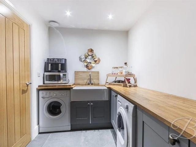 The utility room is a practical and well-appointed space, featuring matching cabinetry, along with a traditional Belfast sink that adds a touch of character. There is ample space and plumbing for both a washing machine and dryer, making everyday tasks convenient.