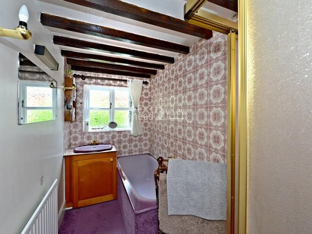 Next stop is the ground-floor bathroom, which boasts a purple bath, partly tiled walls, ceiling beams and a purple wash hand basin built into a vanity unit.