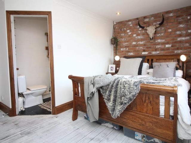 Time to go upstairs now to check out the primary bedroom, which has exposed wooden flooring and a feature brick-style wall. To the left are en suite facilities.