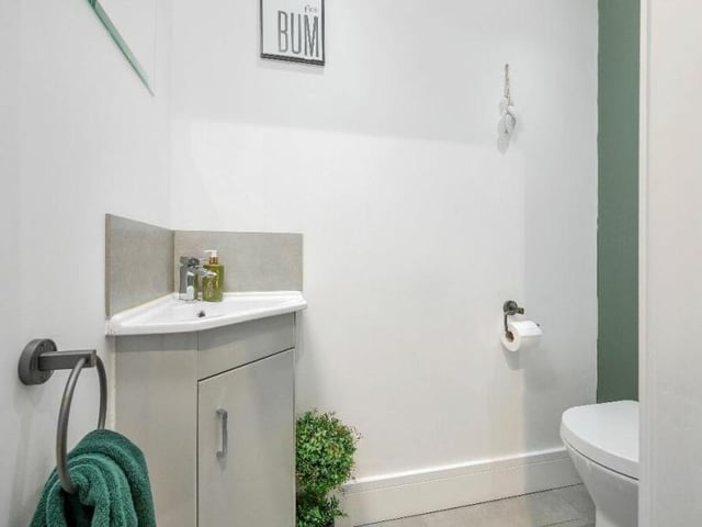 A handy downstairs toilet features a low-flush WC and corner wash hand basin with chrome mixer tap. There is also a radiator and ceiling lighting.