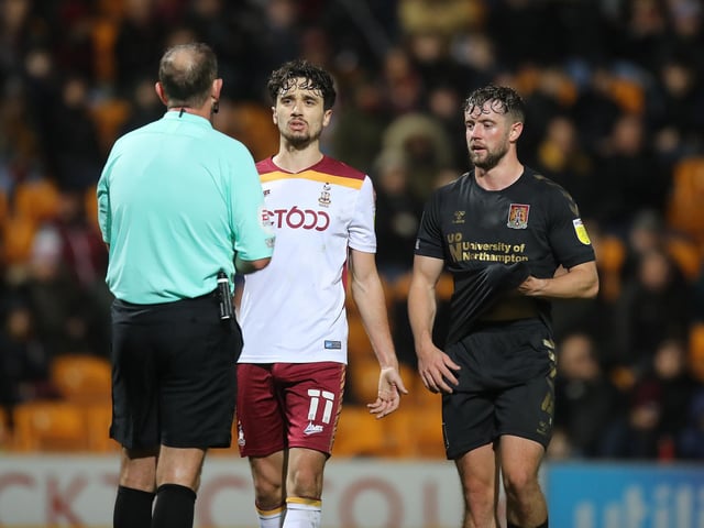 Referee Carl Boyeson shows Jack Sowerby of Northampton Town and Alex Gilliead of Bradford City a yellow card.