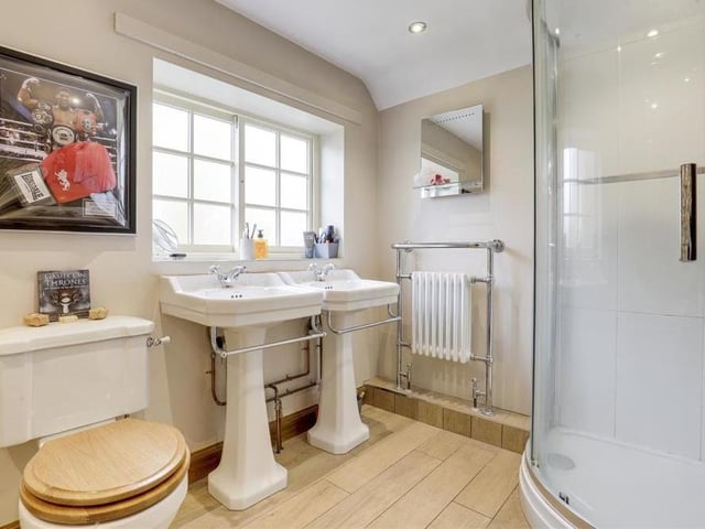 The bathroom also features two period-style pedestal wash basins with chrome towel-rails, and a corner shower enclosure with an overhead rainfall shower and hand-held shower head. A column radiator, recessed spotlights and an opaque, wood-framed sash window are additional assets.
