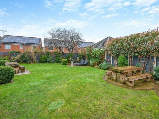 The central lawn in the rear garden is surrounded by well-stocked borders containing a variety of plants and shrubs. Note also a couple of lovely seating areas.
