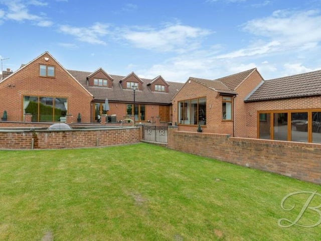Outside the property is a wraparound garden that includes a large, well-maintained lawn and patio with seating area.