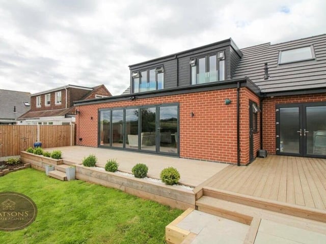 A close-up of the two bedroom balconies on the first floor and the huge bi-folding doors on the ground floor that open out on the garden, where steps lead down to the lawn.