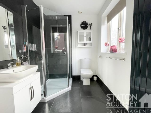 One of the bedrooms on the first floor has access to an en suite shower room. It features a shower cubicle, vanity unit with top-mounted sink and mixer tap, low-level WC, tiled floor, built-in storage cupboard and vertical radiator.