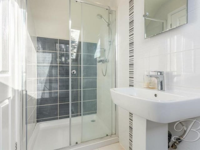 Here is the en suite shower room to the second bedroom on the second floor. A compact space, it includes an enclosed shower, low-flush WC, pedestal sink, full-height tiling and a Velux window.