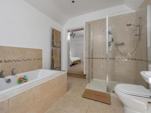 A second shot of the master bedroom's en suite, which comprises a tiled inset bathtub, separate walk-in shower, pedestal wash hand basin with mixer tap, and low-flush WC.