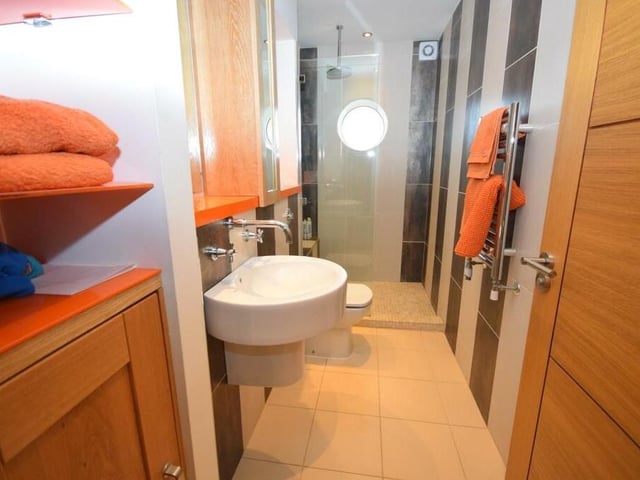 Here is the smart en suite shower room by the bedroom on the ground floor. It comprises a double shower cubicle, low-flush WC and wash basin with storage surround. A polished, tiled floor, underfloor heating and characterful circular window add to its style.