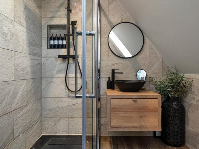 Completing the first floor is this sleek and modern shower room. A three-piece suite includes a walk-in shower enclosure with a matte black, internally plumbed shower, plus a floating wood-effect vanity unit with matte black wash hand basin and mixer tap.