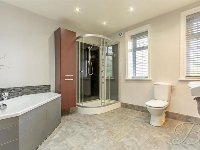 The smart family bathroom consists of a modern, enclosed shower, corner bath, low-flush WC, vanity units, wash hand basin, illuminated vanity mirror, tiled flooring and downlights.