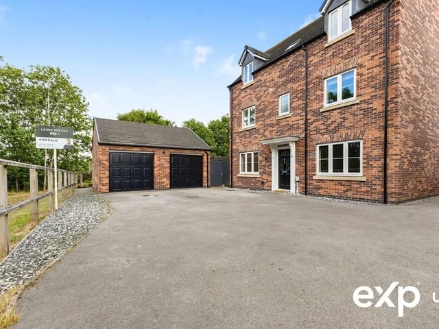 Set back from the road at the bottom of a wide private driveway with ample parking for multiple vehicles, leading to a versatile twin-door double garage.