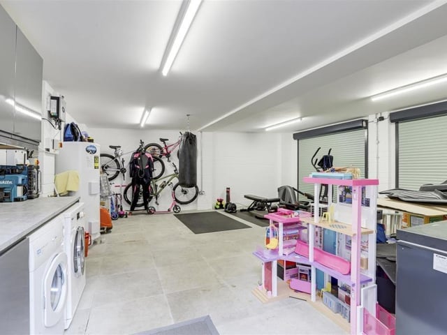 A peek inside the double garage reveals that there is space and plumbing for a washing machine, as well as space for a tumble dryer. It also includes a range of fitted base and wall units with a worktop, tiled flooring and ceiling strip lights.