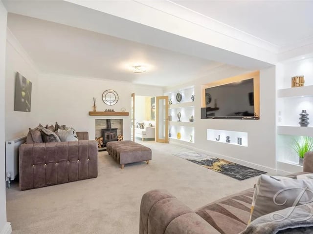 The main reception room is generously sized and features plush carpet, a central heating radiator, a striking feature wall, and a cosy log burner fireplace