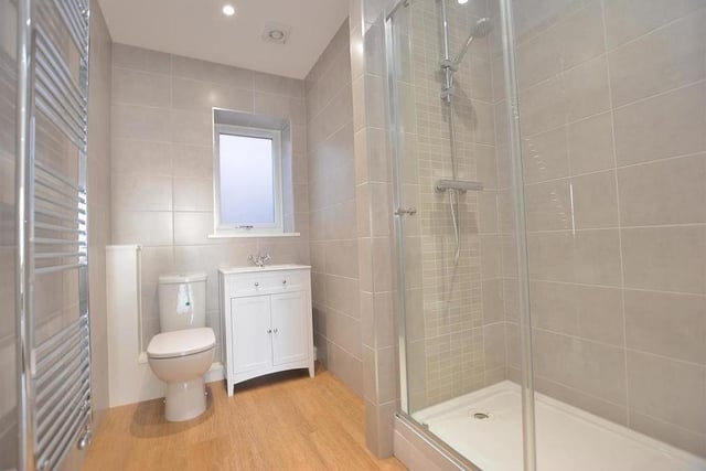 Here is the stylish shower room, which houses a contemporary three-piece suite with chrome fittings. There's a double-width, tiled shower enclosure, a vanity unit with inset wash hand basin, mixer tap and storage cupboard underneath, and a low-flush WC. Completing the room are a large floor-to-ceiling heated towel-rail, fully tiled walls and four ceiling spotlights.