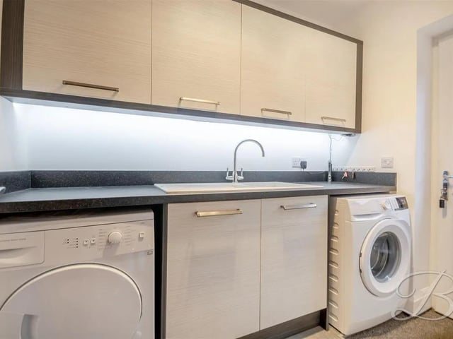 A practical utility area featuring matching cabinetry and worktops, with space for appliances and a door leading to side access.