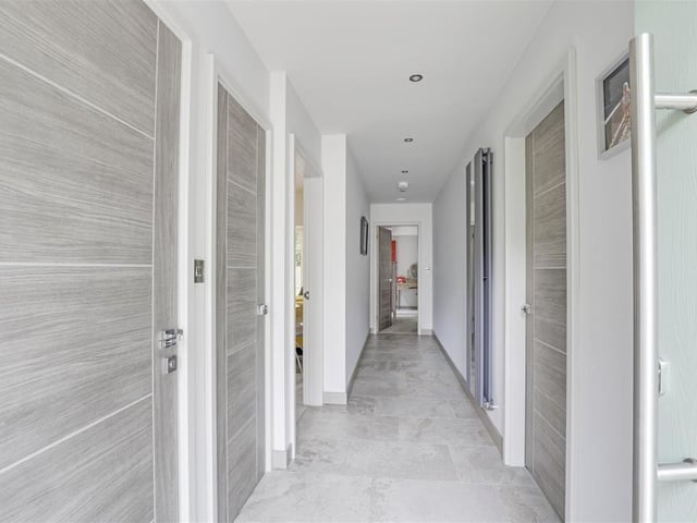 The long entrance hallway that links most of the rooms in the £750,000 bungalow. It has tiled flooring, recessed spotlights, an in-built cloak cupboard, vertical radiator and a wall-mounted security alarm.
