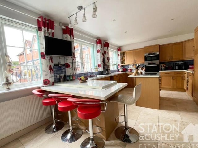 The kitchen/diner has a travertine marble tiled floor below and spotlights above. Integrated appliances include an electric oven, microwave, heated drawer, induction hob, dishwasher and fridge.