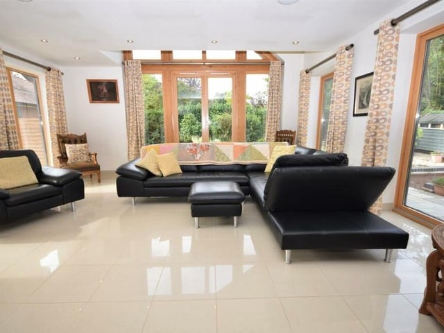 And so we step into the modern lounge, or living room, which boasts numerous features, including a lofty, vaulted ceiling, with incredible glass surround to take advantage of its setting and give views of the beautiful, landscaped grounds.