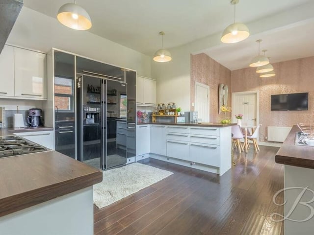 The kitchen oozes style, with gloss wall and base units, a breakfast bar, a free-standing cooker with extractor fan, work surfaces and inset sink with mixer tap. In the background, you can see a dining area.