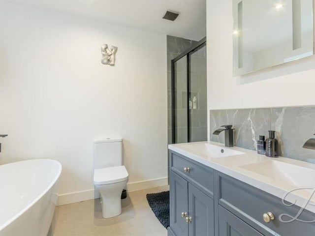 Here is the en suite bathroom to the master bedroom. It is fitted with a free-standing bath, low-flush WC, enclosed shower, and a double vanity unit, with wash hand basins and matte black mixer taps above.
