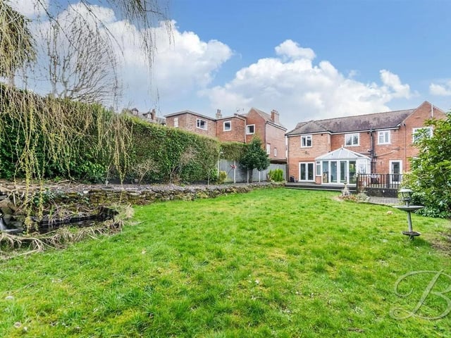 The garden features a spacious lawn, mature shrubs, a decorative pond, and a lovely decked seating area.