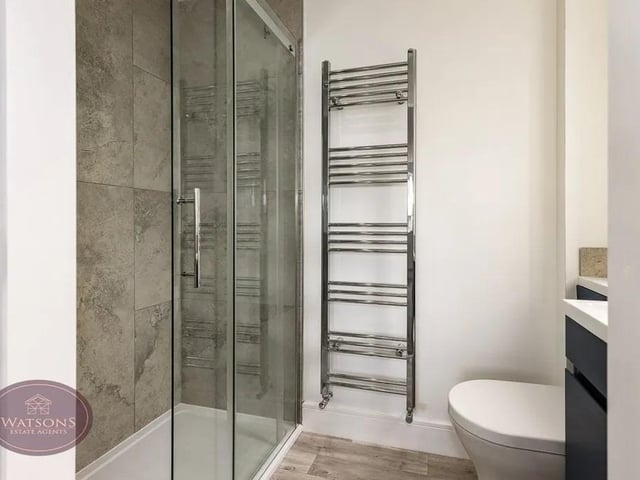 White 3 piece suite comprising concealed cistern wc, vanity sink unit and shower cubicle with mains fed rainfall shower. Chrome heated towel rail, ceiling spotlights and obscured uPVC double glazed window to the side.