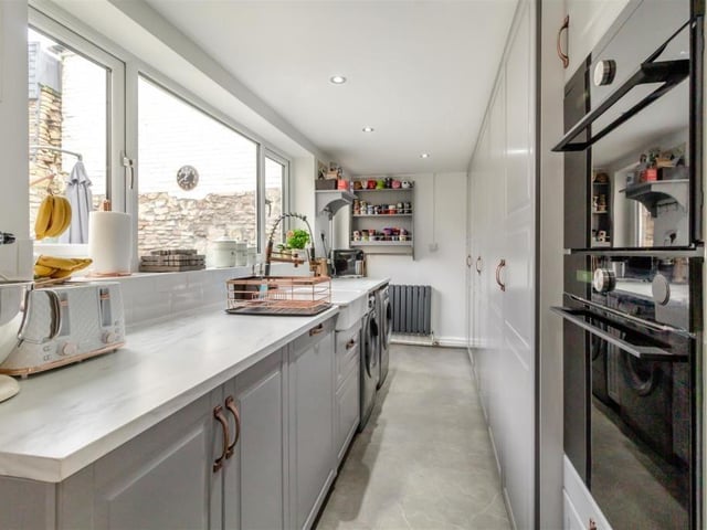 The second part of the kitchen has an integrated combi microwave oven and separate steam oven, with plumbing for a washing machine and space for a tumble dryer. An extensive range of floor-to-ceiling shaker-style cabinets to one wall provide a huge amount of storage, while on the opposite aide of the room is an inset Belfast sink and marble-effect work surfaces.