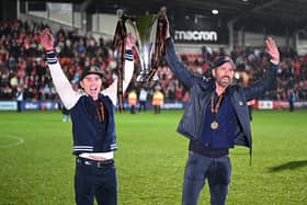 US actor and Wrexham owner Rob McElhenney (L) and US actor and Wrexham owner Ryan Reynolds (R) celebrate on the pitch with the National League trophy after the English National League football match between Wrexham and Boreham Wood at the Racecourse Ground Stadium in Wrexham, north Wales, on April 22, 2023. - Hollywood stars Ryan Reynolds and Rob McElhenney embraced in celebration as they watched Wrexham, who the duo bought in 2020, reach the English Football League for the first time in 15 years on Saturday after a 3-1 win over Boreham Wood. (Photo by Oli SCARFF / AFP) (Photo by OLI SCARFF/AFP via Getty Images)