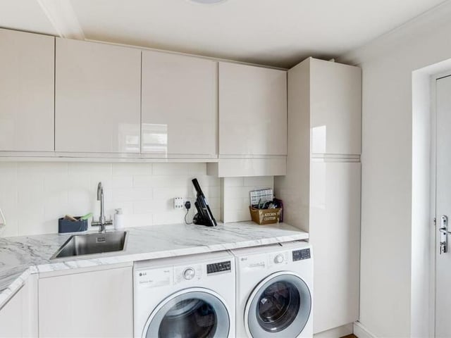 Not far from the kitchen, for added convenience, is this utility room, which has space and plumbing for a washing machine and space for a tumble dryer and fridge freezer. It is fitted with base and wall units, a marble-effect worktop, an undermount sink with swan-neck mixer tap, and also underfloor heating. The door leads to the garden.