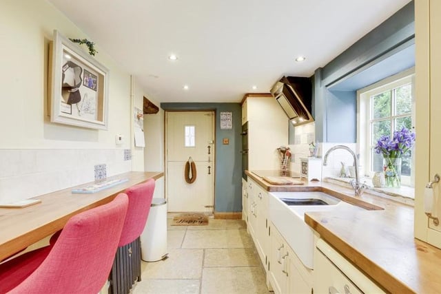The kitchen boasts a range of fitted, shaker-style base and wall units with wooden worktops. Additional assets include flagstone flooring, recessed spotlights, a cast-iron column radiator, two wood-framed sash windows and a stable door,